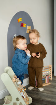 Two toddlers playing with Tix&Mix magnetic toys on a grey wall decal.