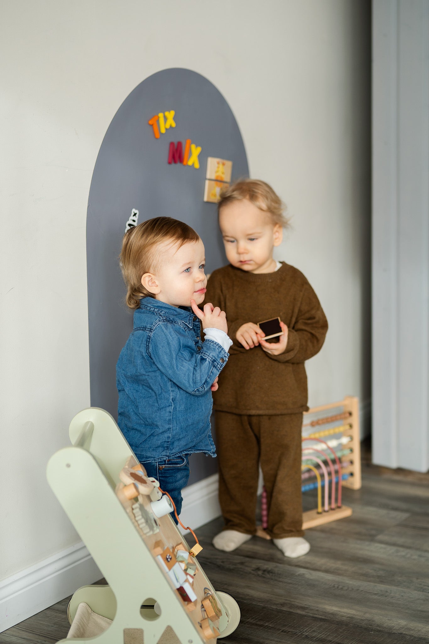 Two toddlers playing with Tix&Mix magnetic toys on a grey wall decal.
