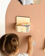 A female toddler drawing on a brown magnetic wall decal featuring the Magic box secured properly on the wall decal.