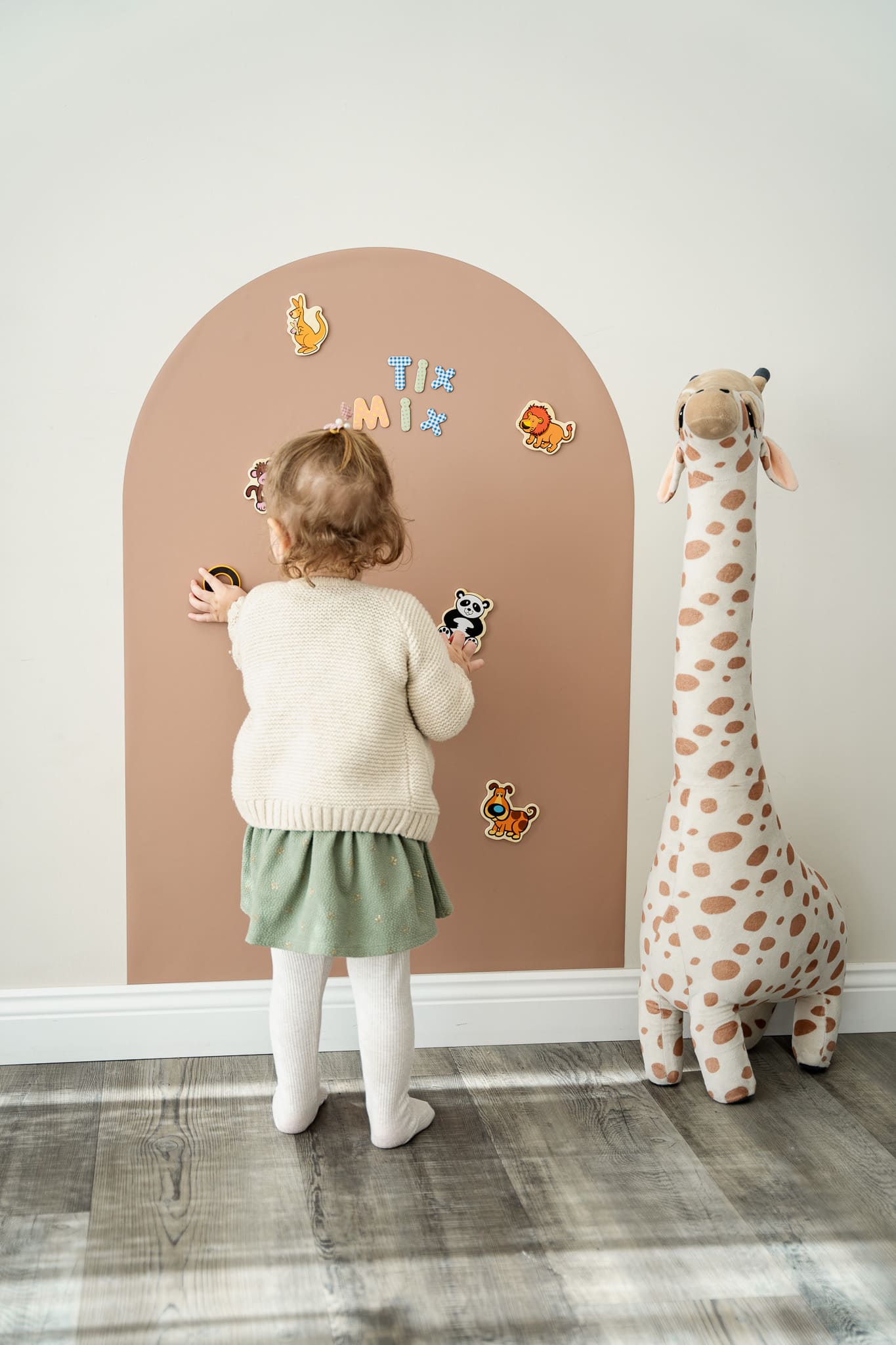 A female toddler playing with Tix&Mix animals toy set on a premium magnetic board attached on the clean white wall.
