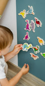 A toddler playing with Tix&Mix magnetic dinosaur set on a cyan blue magnetic wall decal.