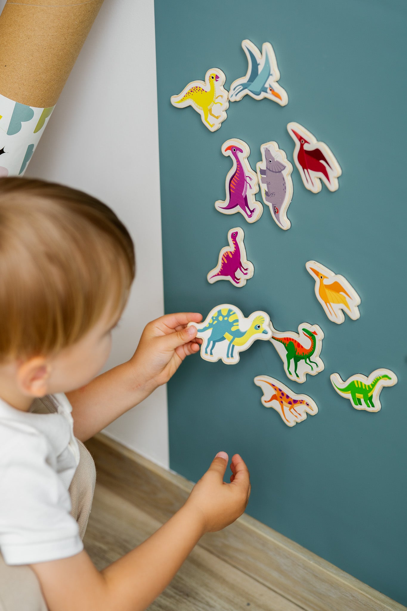 A toddler playing with Tix&Mix magnetic dinosaur set on a cyan blue magnetic wall decal.