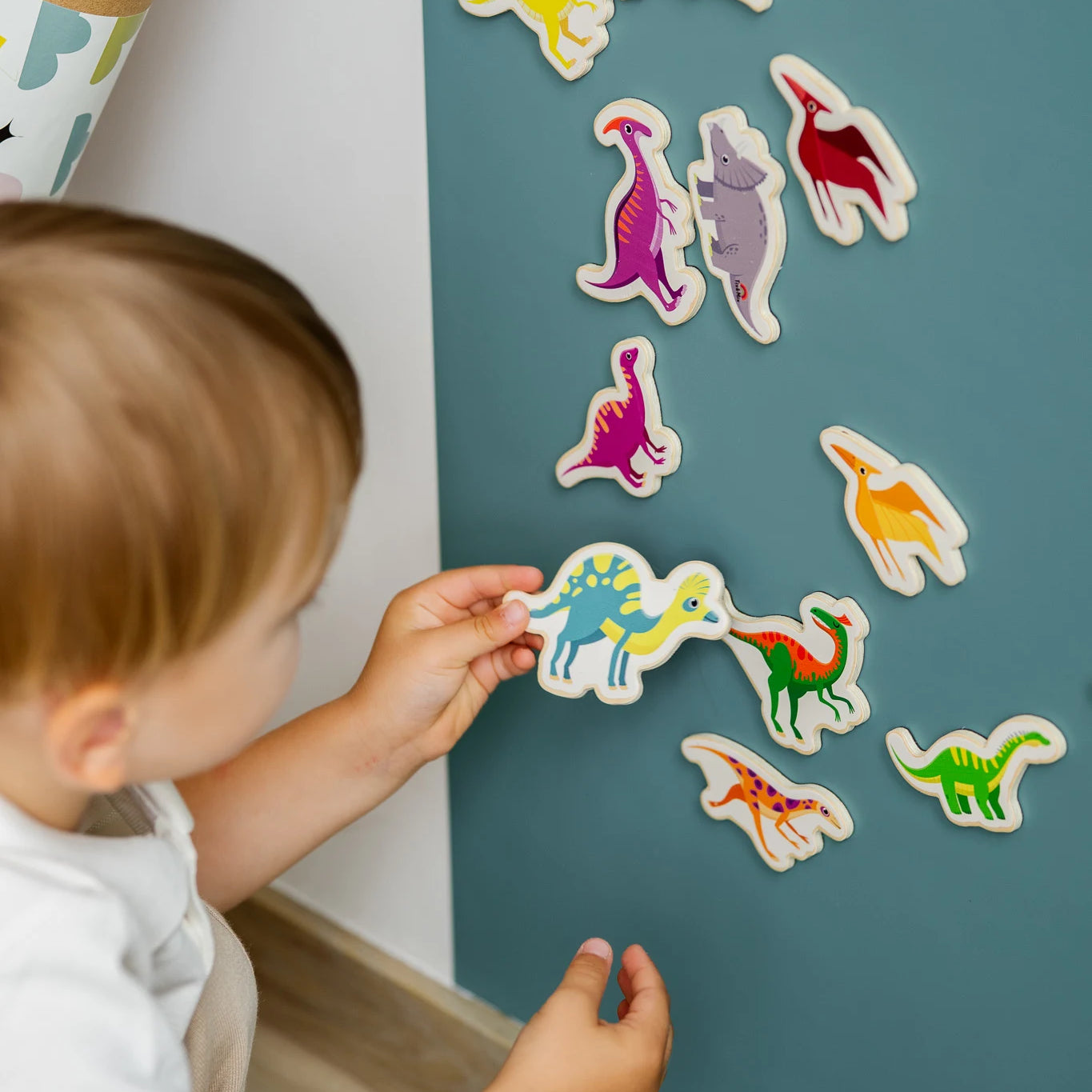 A toddler playing with Tix&Mix magnetic dinosaur toys on a cyan wall decal.