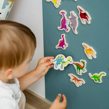 A toddler playing with Tix&Mix magnetic dinosaur toys on a cyan wall decal.