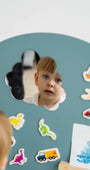 A male child looking at his reflection on a Tix&Mix magnetic mirror on a cyan wall decal.