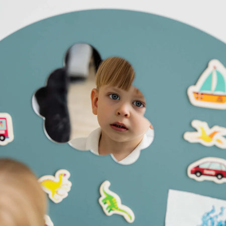 A male child looking at his reflection on a Tix&Mix magnetic mirror on a cyan wall decal.