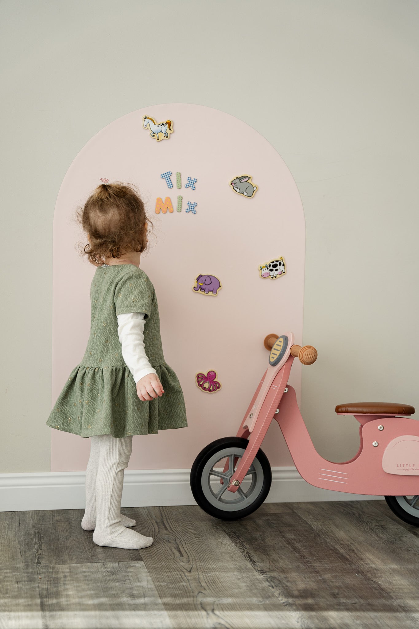 A female toddler playing with Tix&Mix magnetic animals play set on a pink magnetic wall decal.