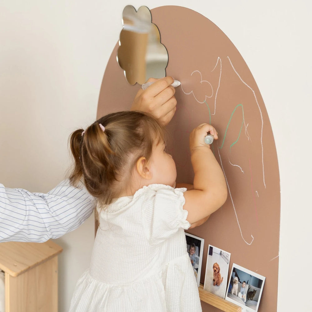 A toddler drawing on a brown magnetic wall decal using a Tix&Mix premium crayon.