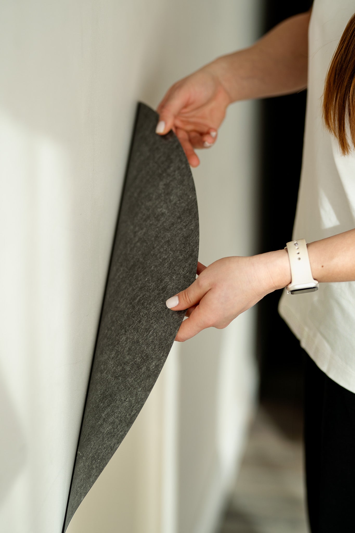 A woman attaching a white magnetic wall decal on a clean white wall.