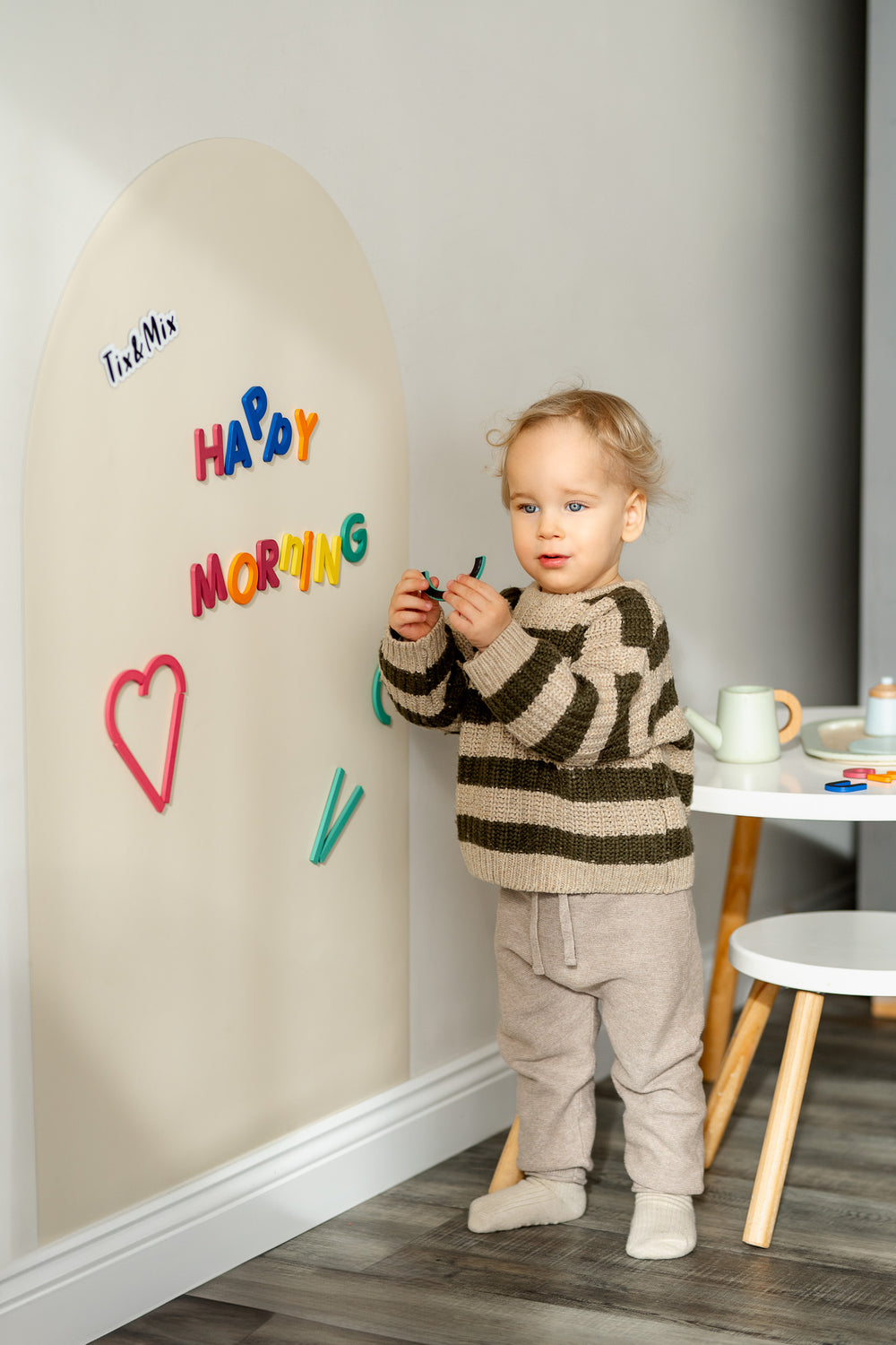A male toddler playing with Tix&Mix Rings and Blocks play set on a white magnetic wall decal.