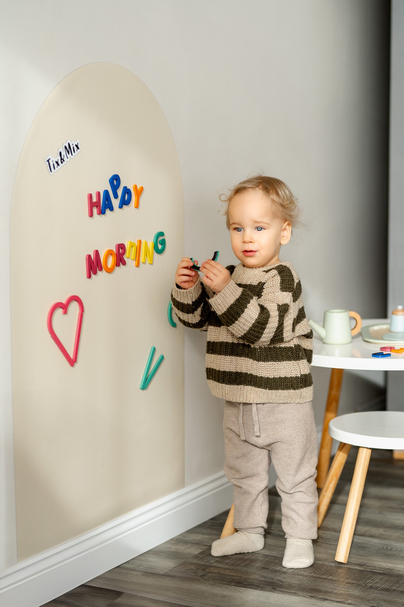 A male toddler playing with Tix&Mix Rings and Blocks play set on a white magnetic wall decal.