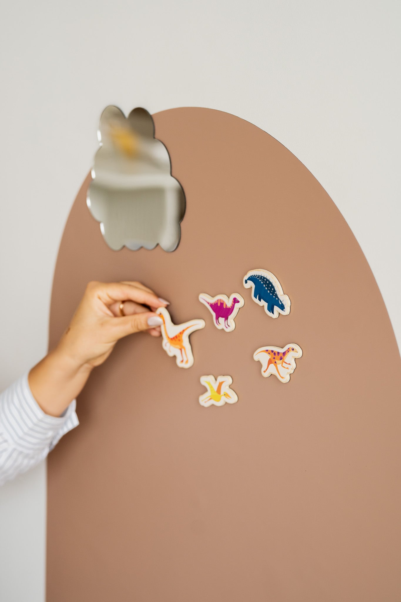 A hand placing Tix&Mix magnetic dinosaur toy on a brown magnetic wall decal.