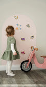 A female toddler playing with Tix&Mix wooden animal toys on a pink magnetic wall decal.