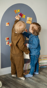 Two toddlers playing with Tix&Mix magnetic animals puzzle set on a premium magnetic grey wall decal.