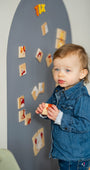 A male toddler playing with Tix&ix animals puzzle toy set on a grey magnetic wall decal.