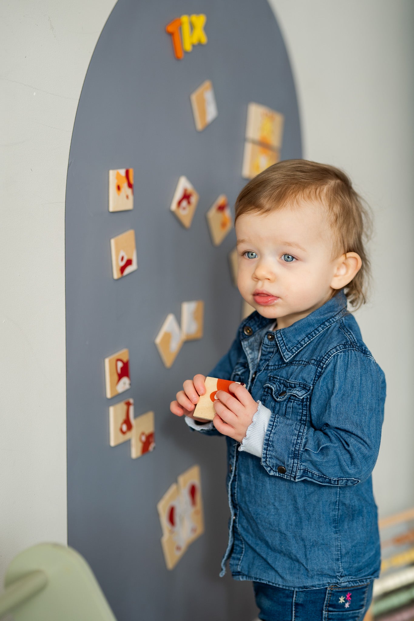 A male toddler playing with Tix&ix animals puzzle toy set on a grey magnetic wall decal.