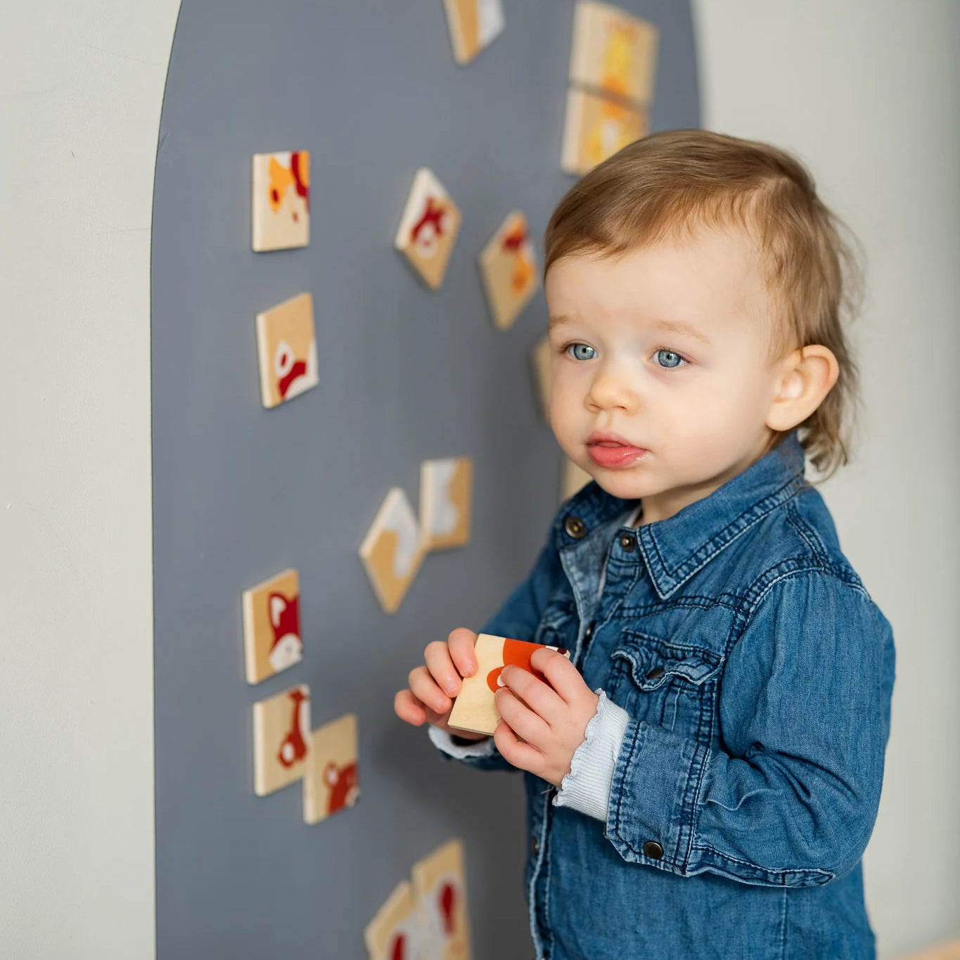 A male toddler playing with wooden magnetic animals puzzle playset on a grey wall decal.
