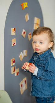 A male toddler playing with wooden magnetic animals puzzle playset on a grey wall decal.
