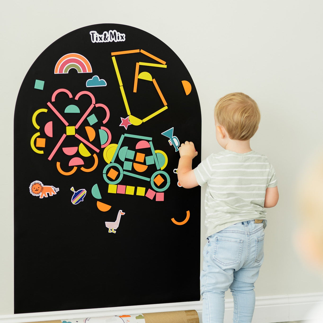 A male toddler playing with Tix&Mix Rings and Blocks Play Kit on a black magnetic wall decal.