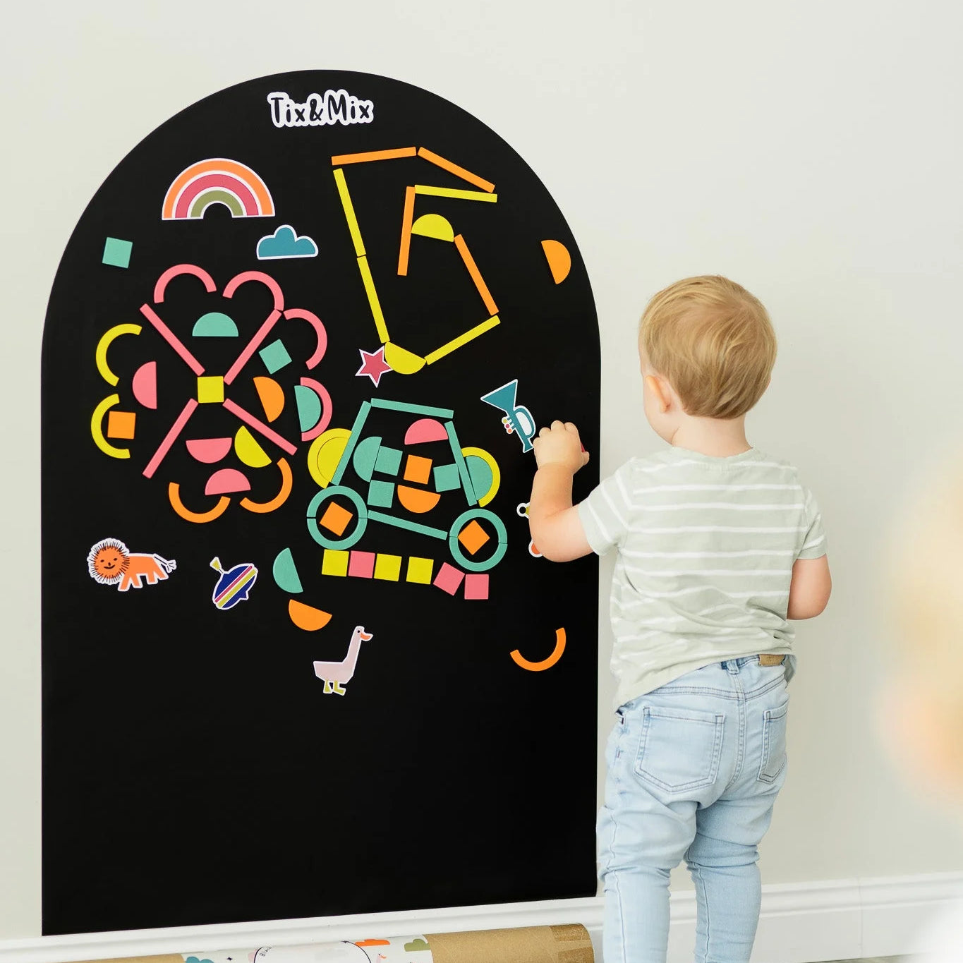 A male kid playing with Tix&Mix rings and blocks on a black magnetic wall decal.