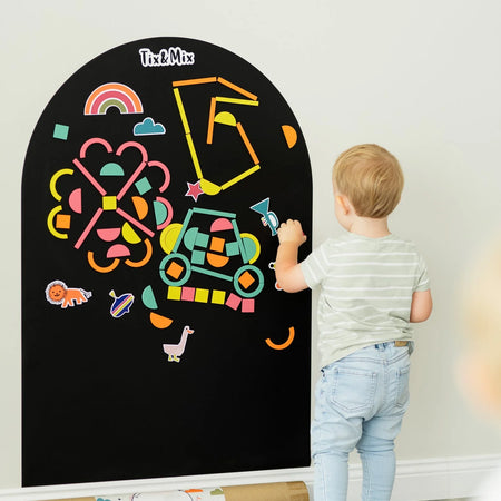 A male kid playing with Tix&Mix rings and blocks on a black magnetic wall decal.