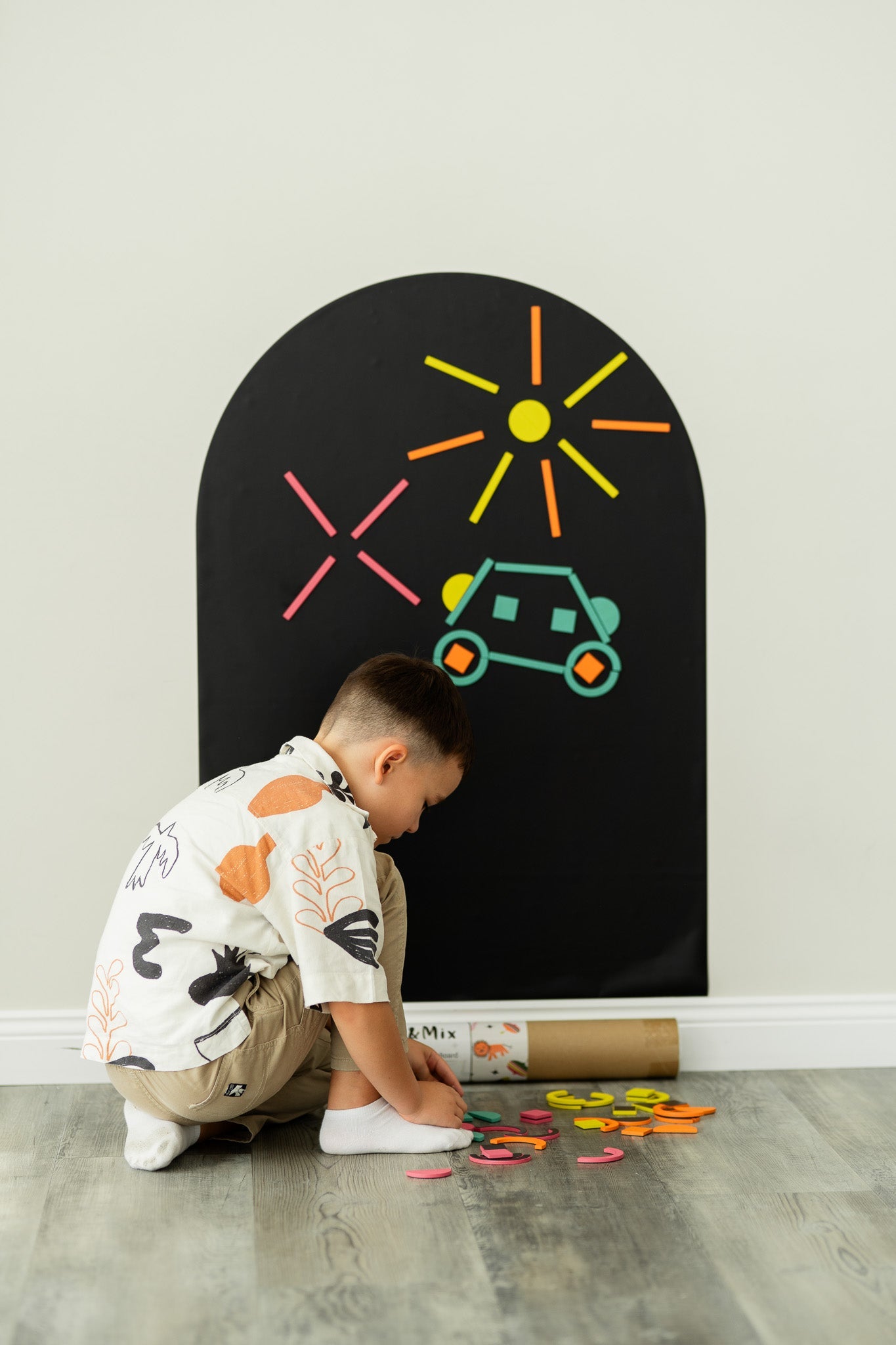 A male kid playing with Tix&Mix rings and blocks play kit on a black magnetic wall decal.