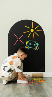 A male kid playing with Tix&Mix Rings and Blocks on a black magnetic wall decal.