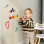 A toddler holding Tix&Mix rings and blocks play set with white magnetic wall decal on the wall.