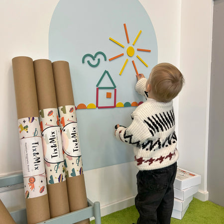 A toddler playing with Tix&Mix Rings and Blocks set on a blue dream wall decal with new decal rolls on the side.
