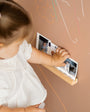 A toddler placing pictures on a Tix&Mix Treasure Shelf secured on a brown magnetic wall decal.