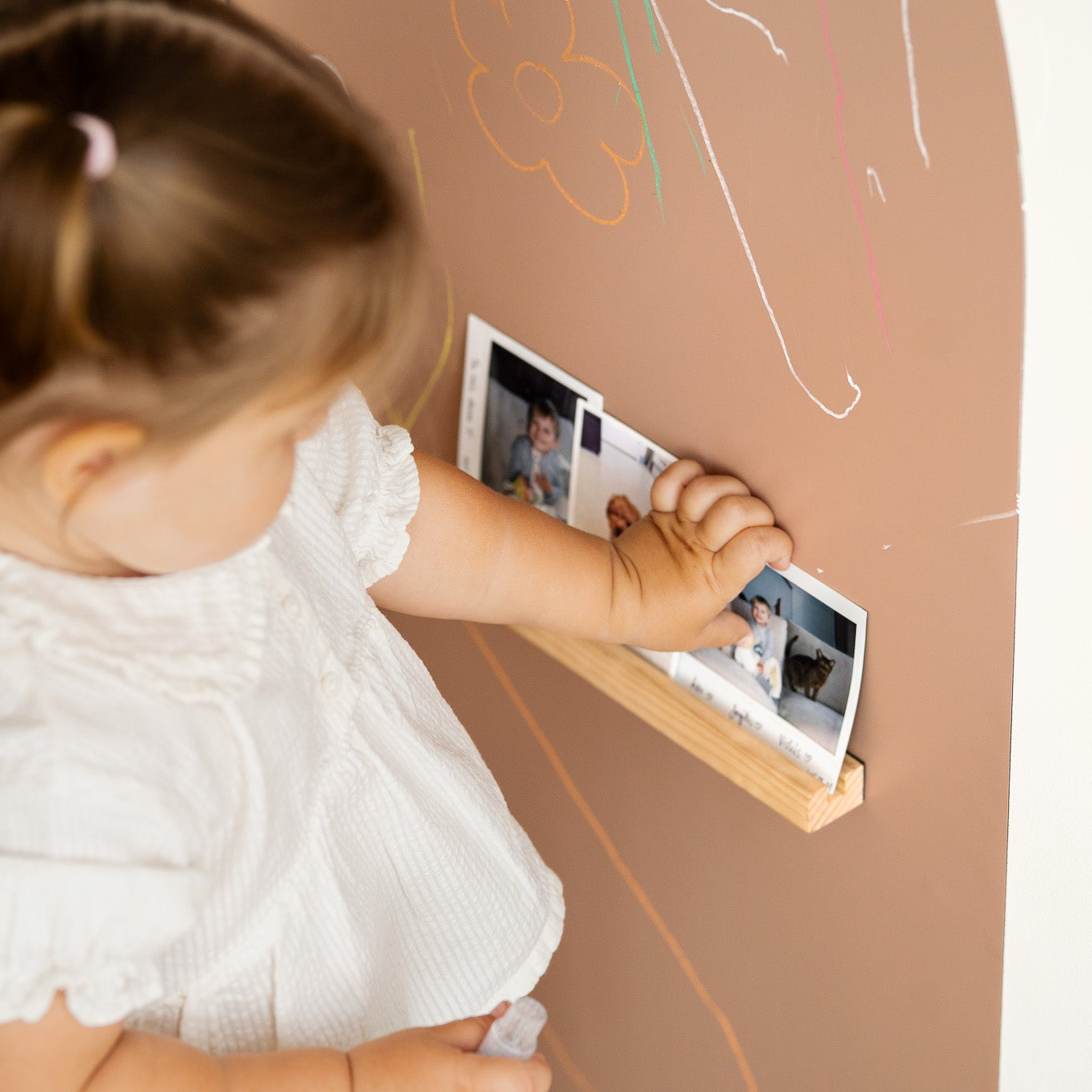 A toddler placing pictures on a Tix&Mix Treasure Shelf secured on a brown magnetic wall decal.