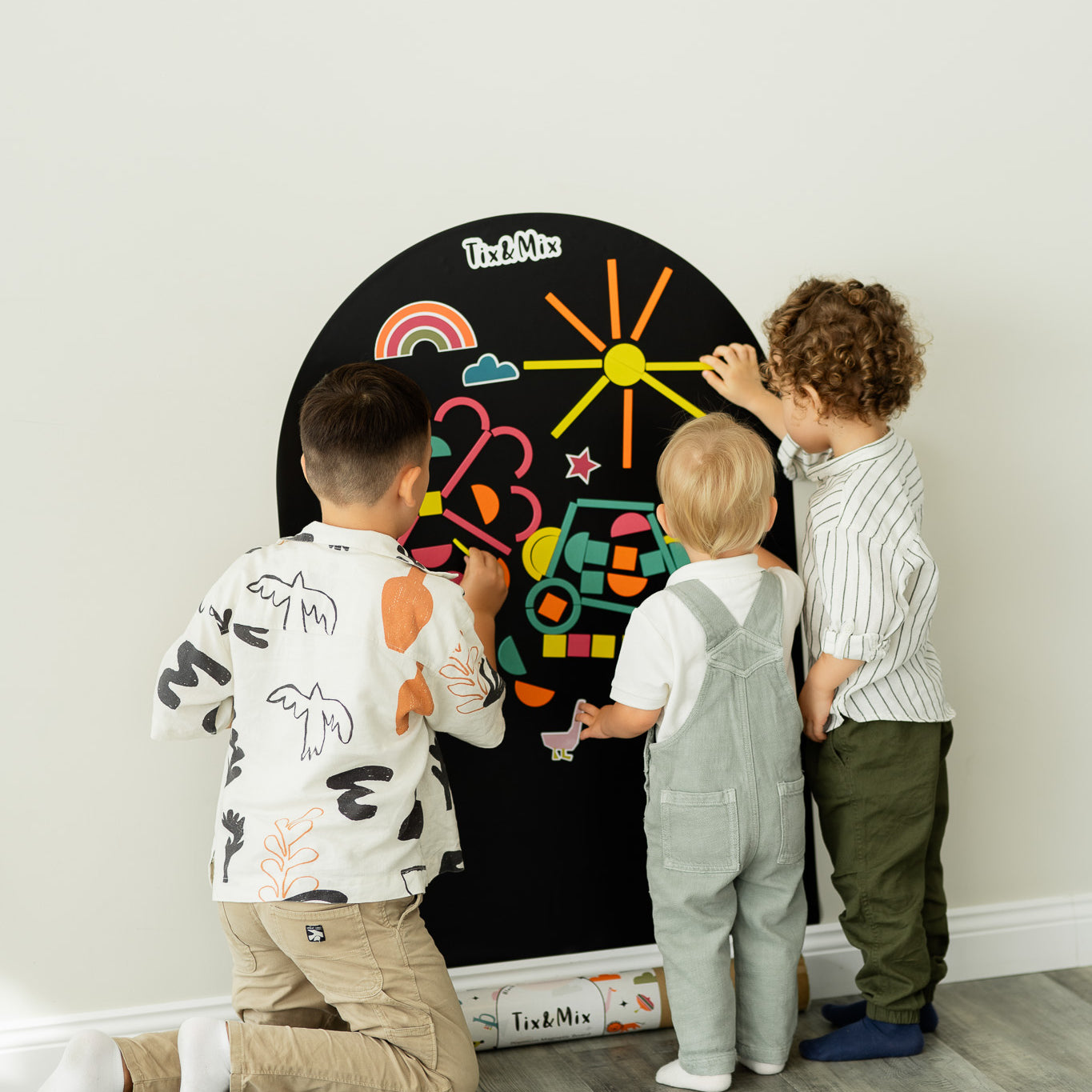 Three kids playing with Tix&Mix rings and block play kit on a black magnetic wall decal.
