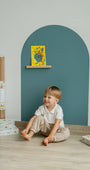 A toddler smiling while sitting in front of Tix&Mix cyan wave magnetic wall decal.