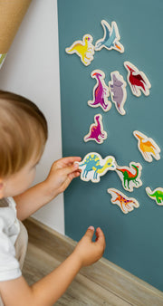 A male toddler playing with Tix&Mix magnetic dinosaur toys on a cyan magnetic wall decal.