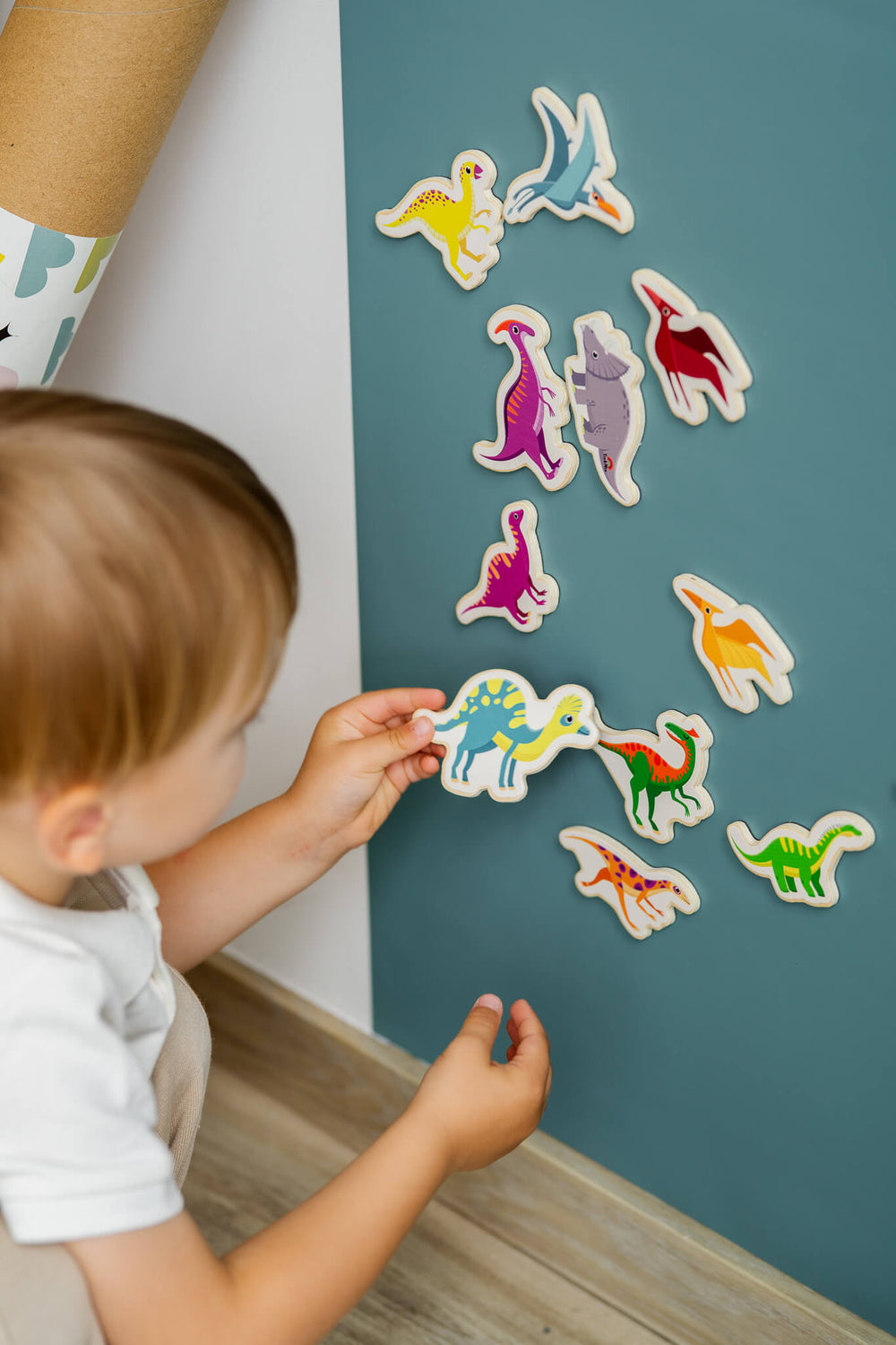 A male toddler playing with Tix&Mix magnetic dinosaur toys on a cyan magnetic wall decal.