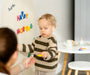 A toddler playing with Tix&Mix magnetic letters toys on a white magnetic wall decal while being assisted by his parent.