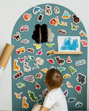 A toddler looking at the Tix&Mix magnetic wooden toys and accessories placed on a cyan wave magnetic wall decal.