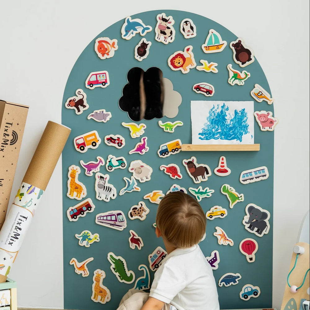 A toddler looking at the Tix&Mix magnetic wooden toys and accessories placed on a cyan wave magnetic wall decal.