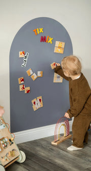 A toddler playing with Tix&Mix wooden magnetic animals puzzle playset on a grey  wall decal.