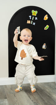 A toddler happily playing with TixMix magnetic toys on a black magnetic wall decal.