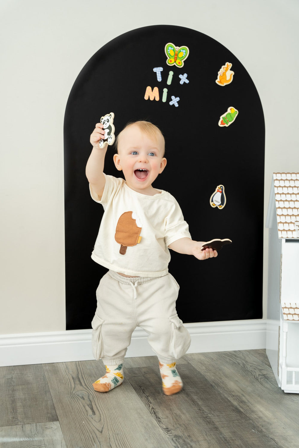A toddler happily playing with TixMix magnetic toys on a black magnetic wall decal.