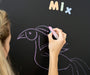A female person drawing a bird on a Tix&Mix magnetic wall decal using a purple crayon.