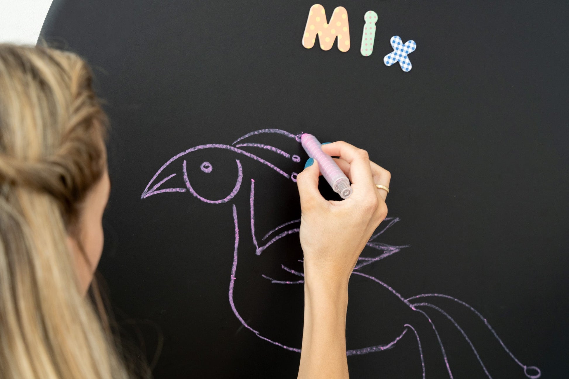 A female person drawing a bird on a Tix&Mix magnetic wall decal using a purple crayon.
