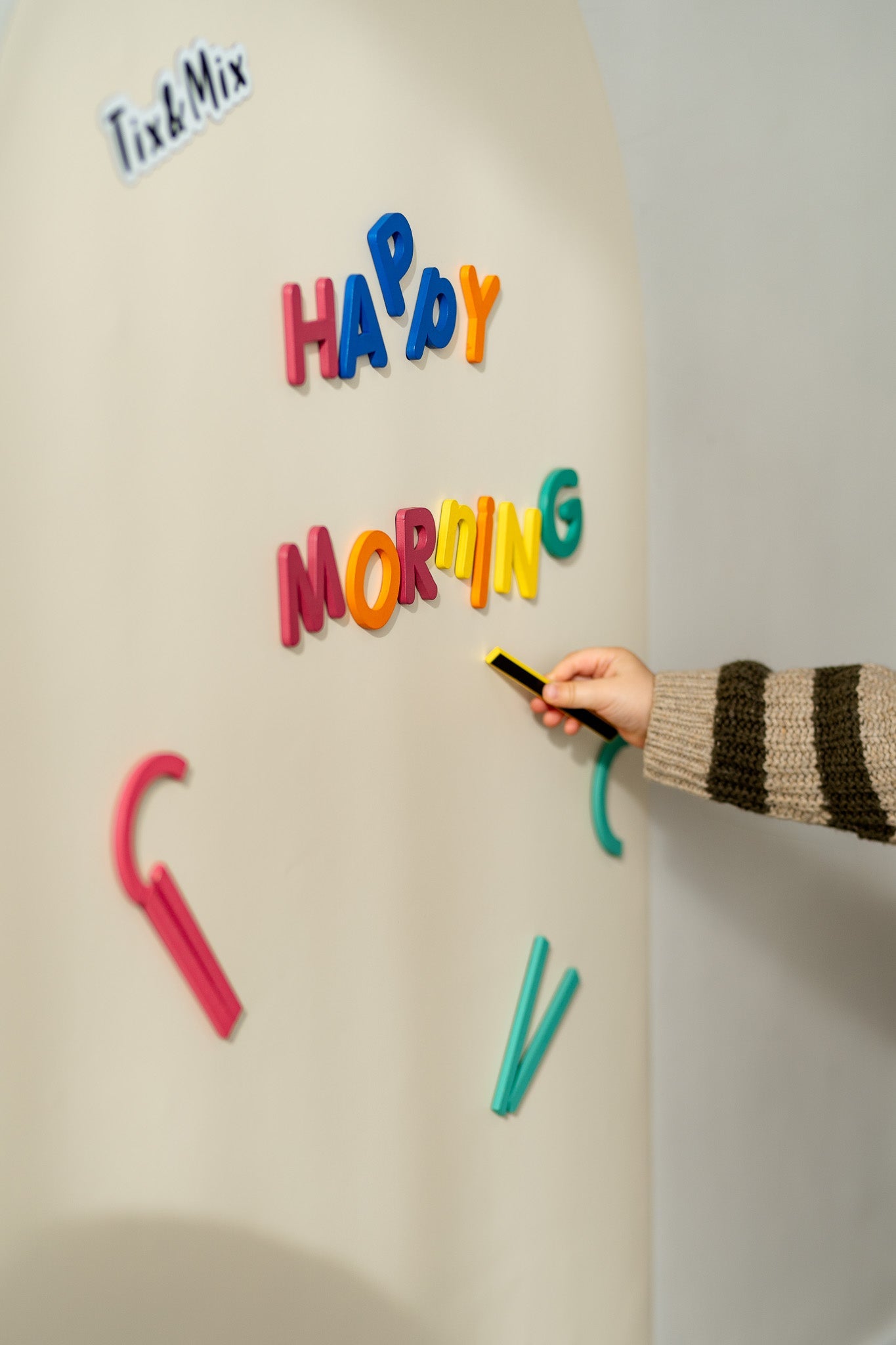 A hand placing rings and blocks set on a white magnetic wall decal.