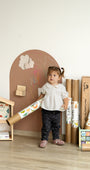 A toddler holding a Tix&Mix magnetic wall decal roll in a playroom, standing beside a brown wall board.
