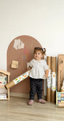A female toddler standing in front of Tix&Mix brown magnetic wall decal featuring wall decal rolls located at the side.
