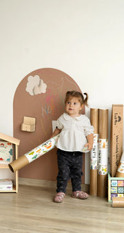 A female toddler standing in front of Tix&Mix brown magnetic wall decal featuring wall decal rolls located at the side.