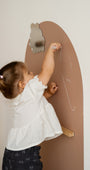 A toddler drawing with chalk on a Tix&Mix magnetic wall decal with a magnetic mirror and treasure shelf.