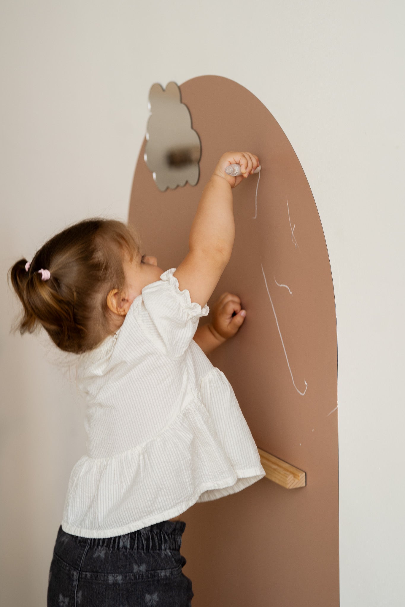 A toddler drawing with chalk on a Tix&Mix magnetic wall decal with a magnetic mirror and treasure shelf.