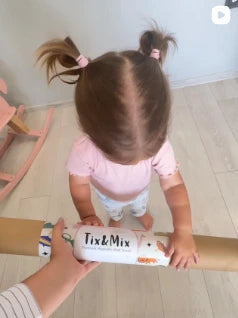 Child holding a box labeled 'Tix & Mix' on a wooden floor.